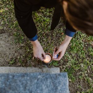 Person lighting a candle at a gravestone in a cemetery, symbolizing remembrance and mourning.