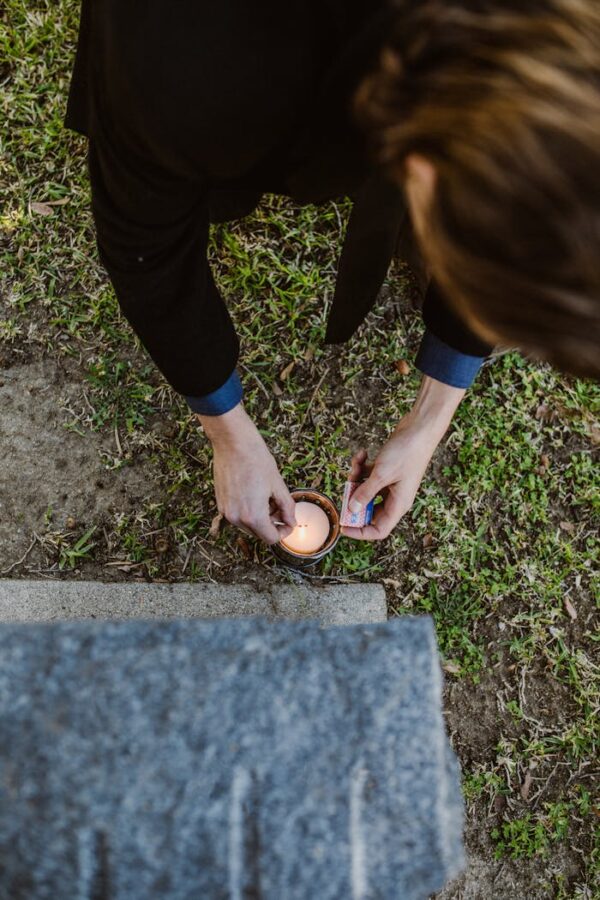 pexels-photo-6841172 Person lighting a candle at a gravestone in a cemetery, symbolizing remembrance and mourning.