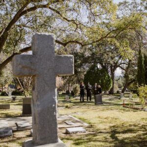 A serene cemetery with a prominent stone cross surrounded by lush greenery and gravestones.