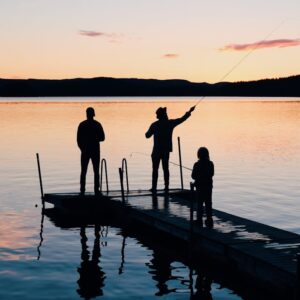 A serene scene of a family fishing together on a lake dock at sunset, creating silhouettes on the water.