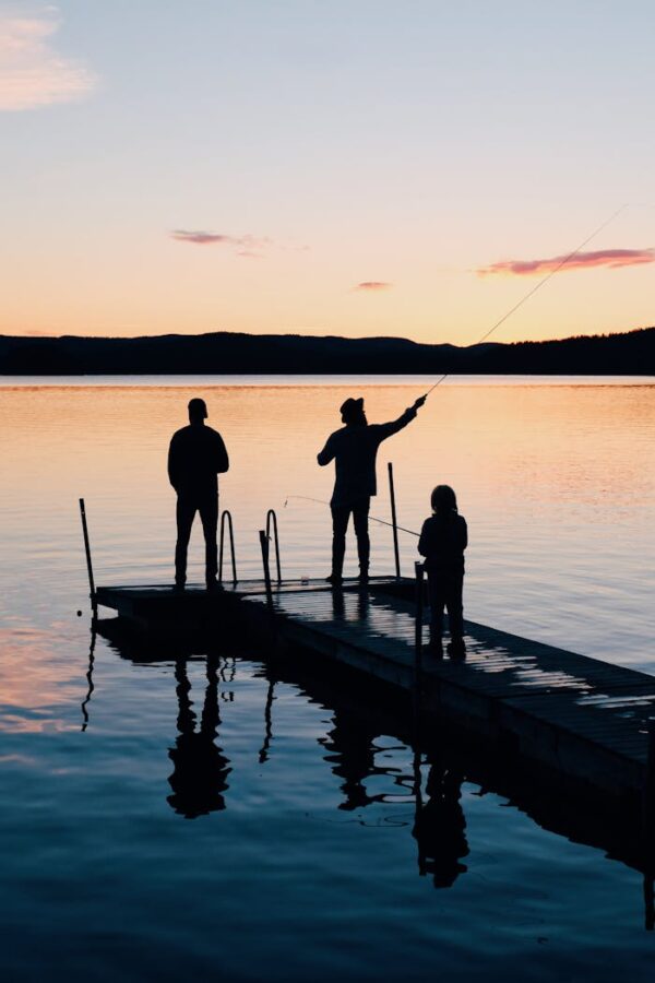 pexels-photo-988622 A serene scene of a family fishing together on a lake dock at sunset, creating silhouettes on the water.